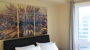 Un cuarto de hotel con una cama, un cuadro abstracto grande en la pared y una ventana con cortinas.