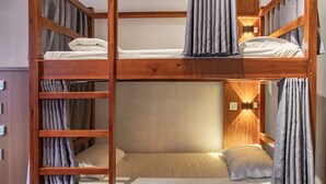 A bunk bed with a wooden frame, a bedside table, and curtains.