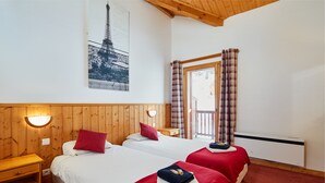 Une chambre avec deux lits, des murs en bois, une fenêtre avec des rideaux à carreaux et un luminaire fixé au mur.