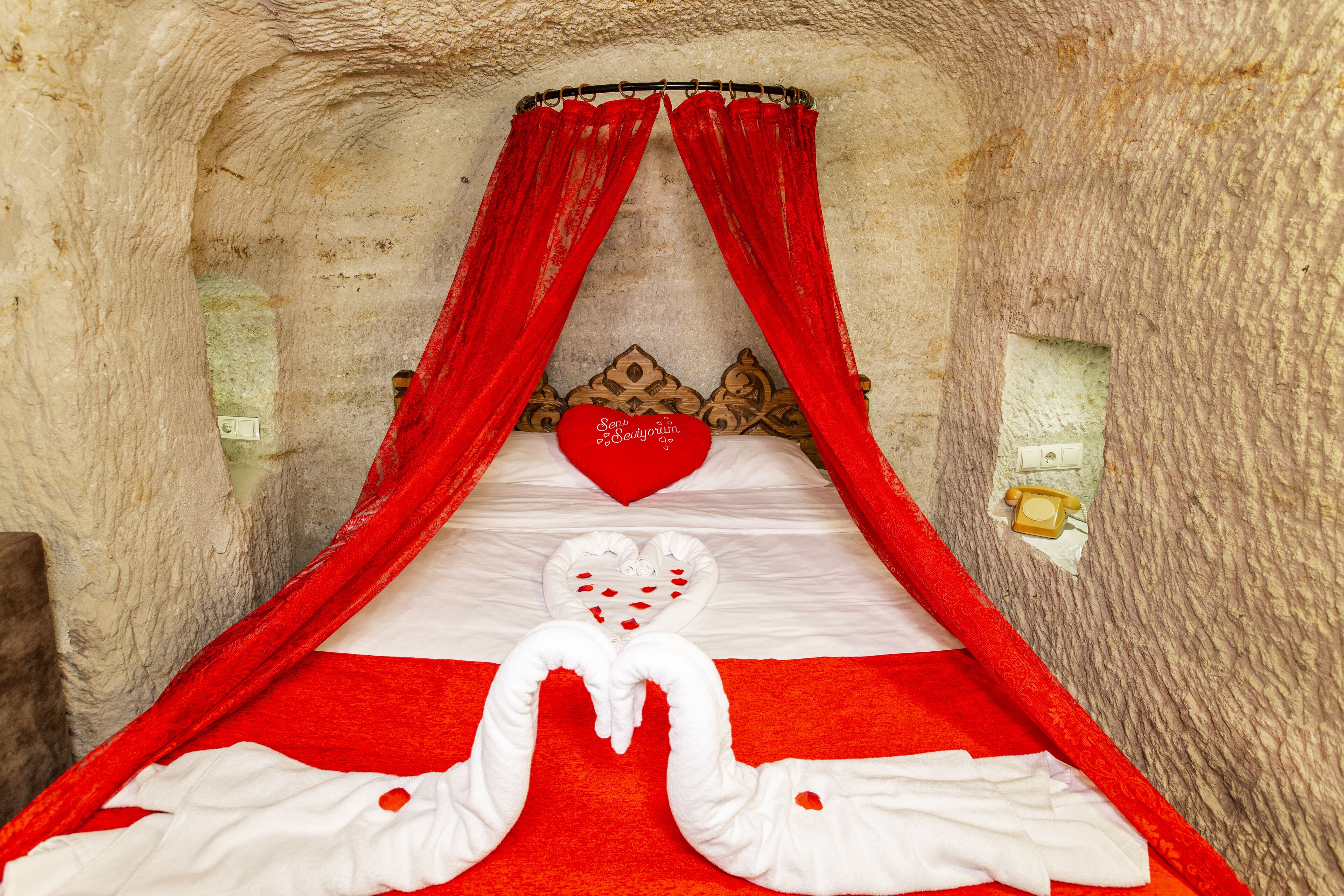 A bed with red and white bedding, a heart-shaped pillow, and a canopy with red drapes.
