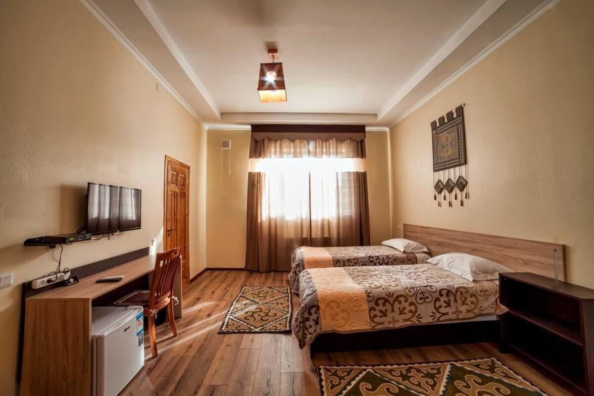 A hotel room with two beds, a desk with a TV, a refrigerator, and a wooden chair.