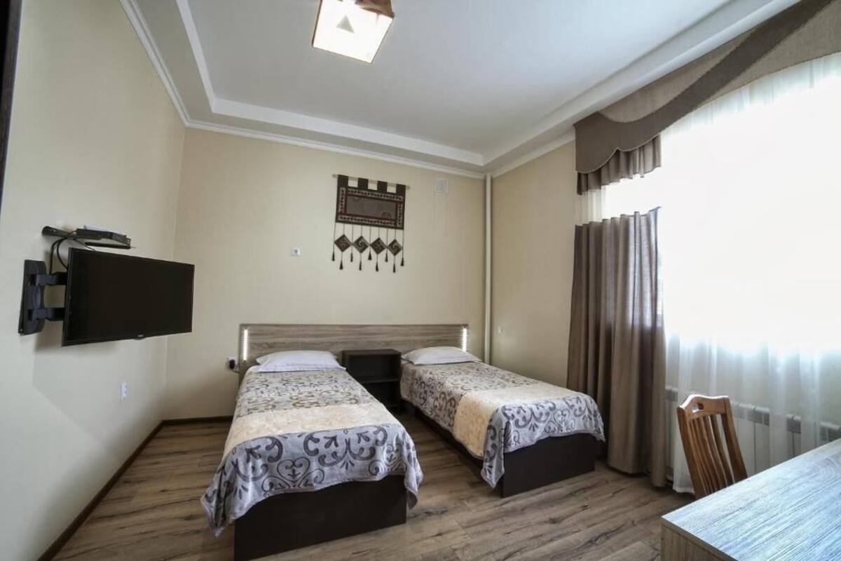 A hotel room with two beds, a flat-screen TV mounted on the wall, a wooden floor, and a window with curtains.