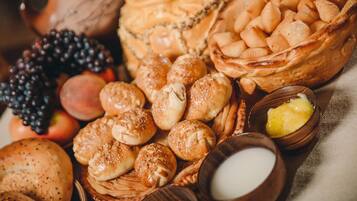 A variety of baked goods including bread, rolls, and pastries, along with some fruits and small bowls containing spreads.