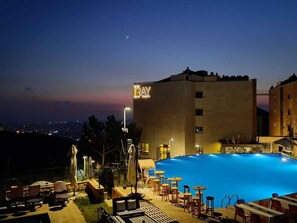A hotel with a rooftop pool, outdoor seating, and a view of the city at dusk. - The Ray Hotel & Studios (Ain Saadeh)
