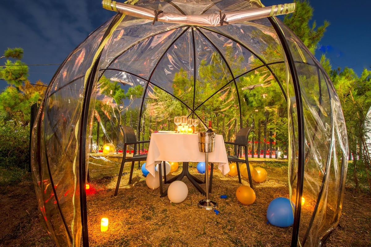 Una struttura a cupola trasparente con un tavolo e sedie all'interno, circondata da palloncini e candele.