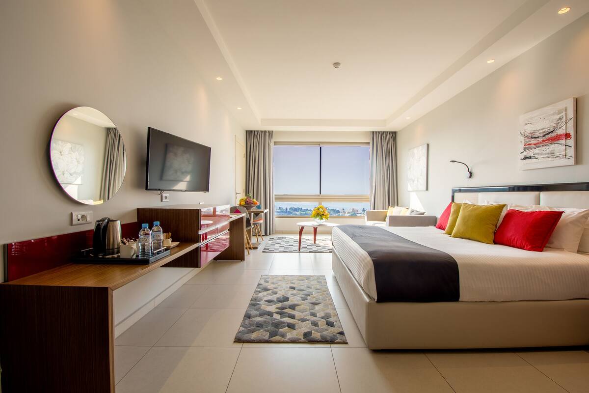 Una moderna camera d'albergo con un letto grande, una scrivania, una TV, uno specchio e vista sulla città.