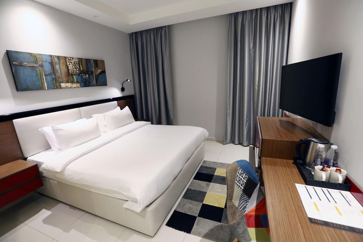 Una camera d'albergo moderna con un letto grande, una TV a schermo piatto, una macchina del caffè e una scrivania con una sedia.