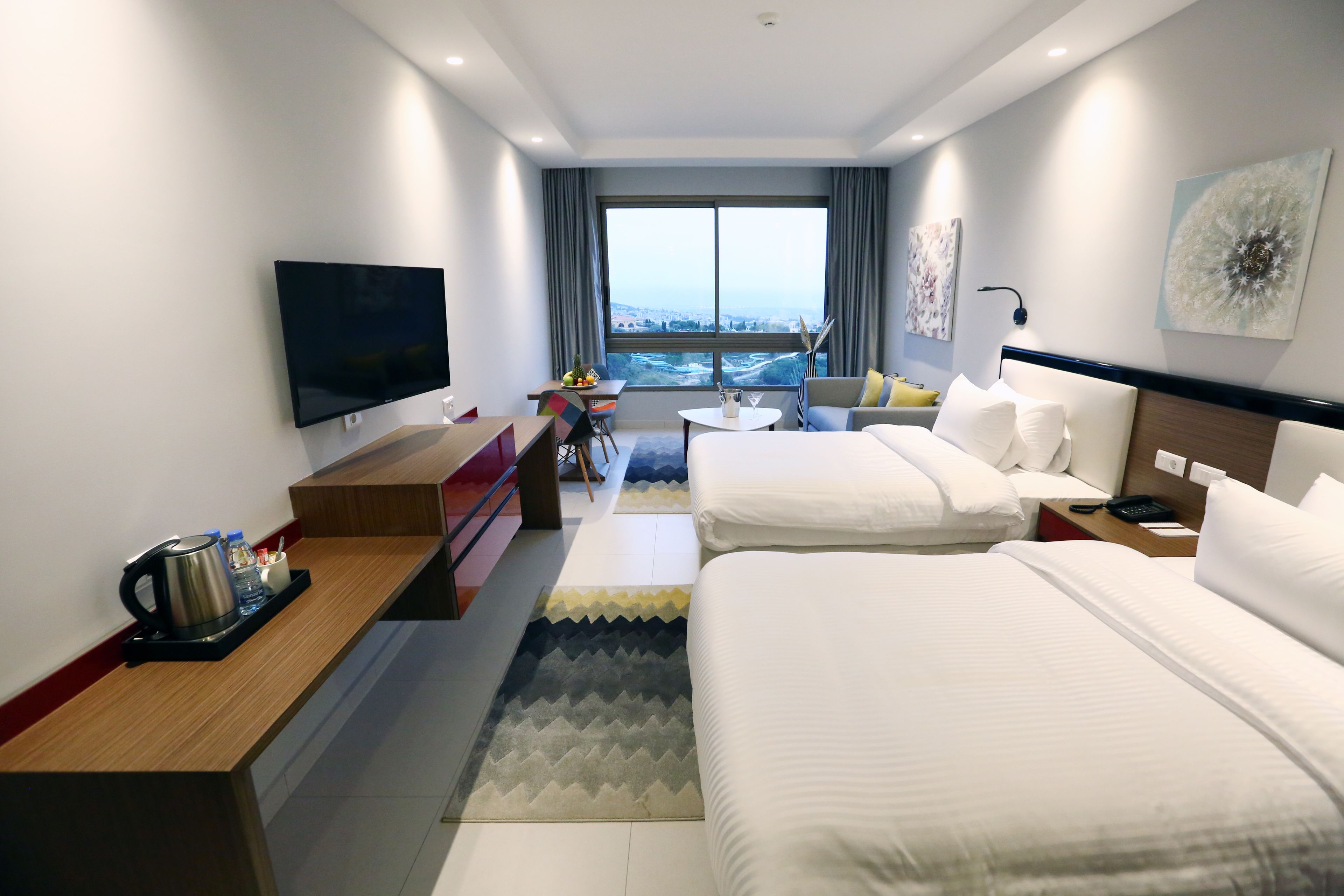 A hotel room with two beds, a TV, a desk with a coffee maker, a small table, and a view of the city.