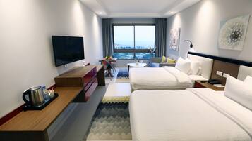 A hotel room with two beds, a TV, a desk with a coffee maker, a small table, and a view of the city.