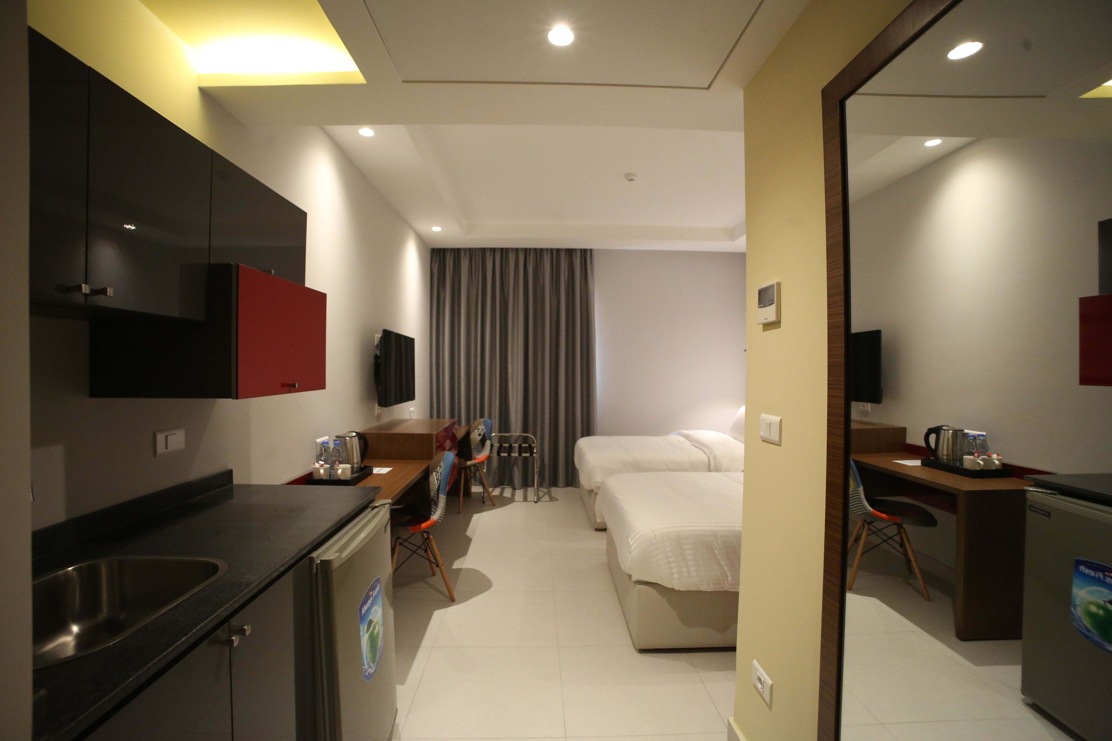 A hotel room with a kitchenette, a bed, a desk, and a TV.