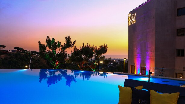 Ein Pool mit Sonnenuntergangsblick, ein Gebäude mit der Aufschrift 'The Ray' und eine Bank mit gelben Kissen.