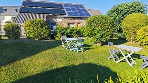 A house with solar panels on the roof, a stone facade, and a well-maintained garden with two tables and chairs. - Chambres d'hôtes Les Salles (Beauvoir)