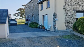 A stone building with a blue roof, a gravel driveway, and a small outdoor seating area with plastic chairs. - Chambres d'hôtes Les Salles (Beauvoir)