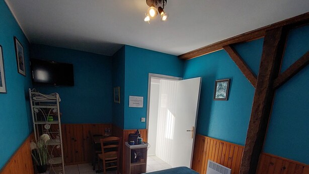 A room with a bed, a desk, a chair, a television, and a door. - Chambres d'hôtes Les Salles (Beauvoir)