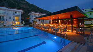 A swimming pool with adjacent outdoor seating and a bar area, surrounded by buildings with balconies.