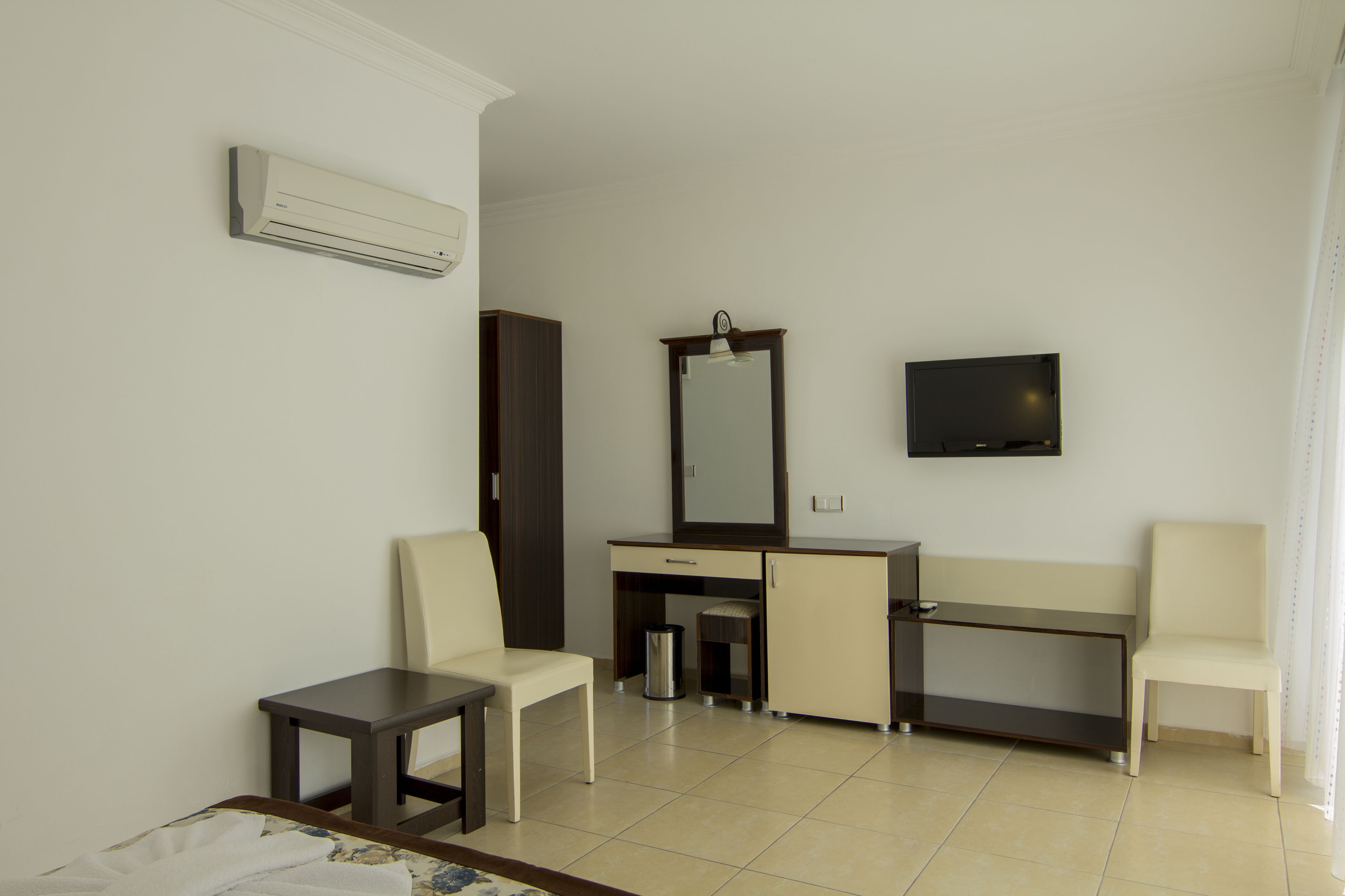 A hotel room with a bed, two chairs, a desk, a television, and an air conditioning unit.