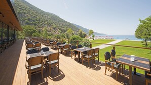 A deck with tables and chairs overlooking a scenic view of a lake and mountains.