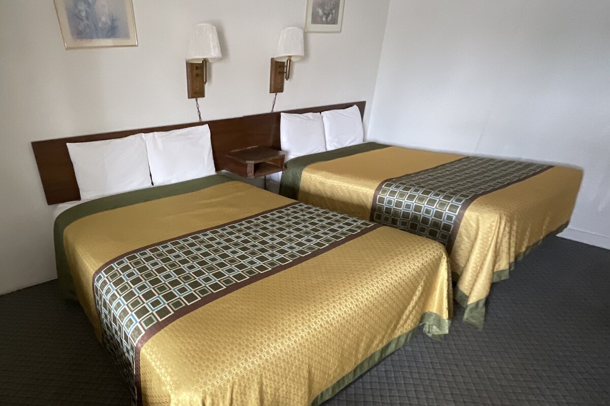 A hotel room with two beds, a wooden headboard, two wall-mounted lamps, and a patterned carpet.