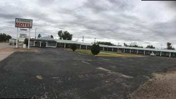 A motel with a large parking lot, a signboard, and a row of rooms with a green roof.