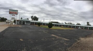 Un motel con un amplio estacionamiento, un letrero y una hilera de habitaciones con techo verde.