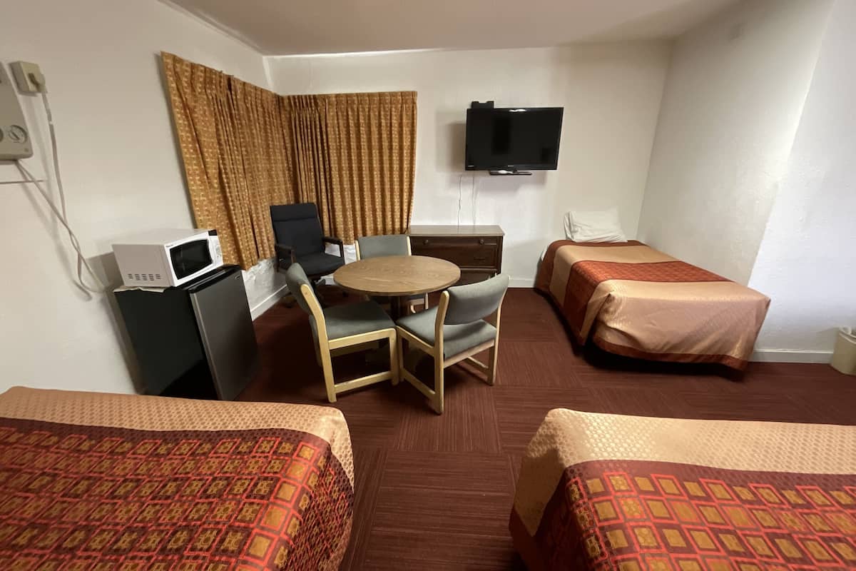A hotel room with two single beds, a desk with a computer, a chair, a small table, a TV mounted on the wall, and a window with curtains.