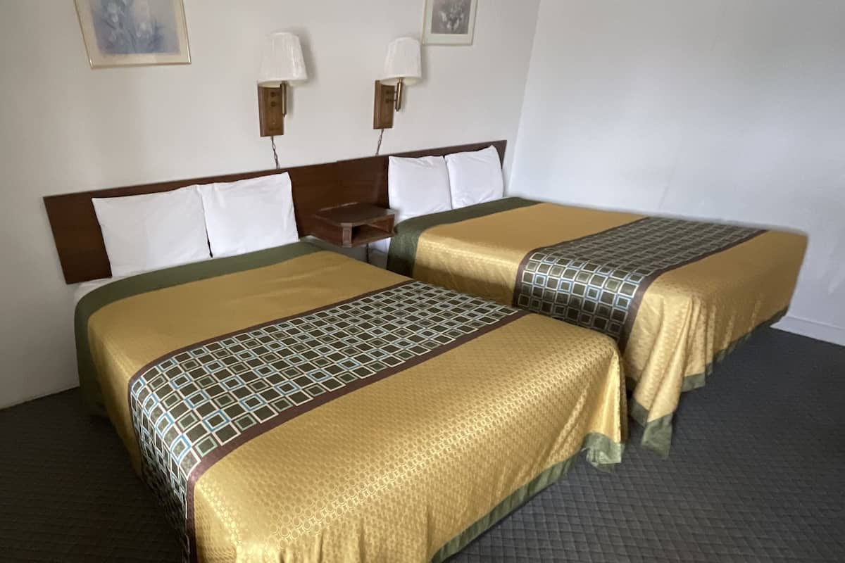 A hotel room with two beds, each with a patterned bedspread, a wooden headboard, and two wall-mounted lamps.