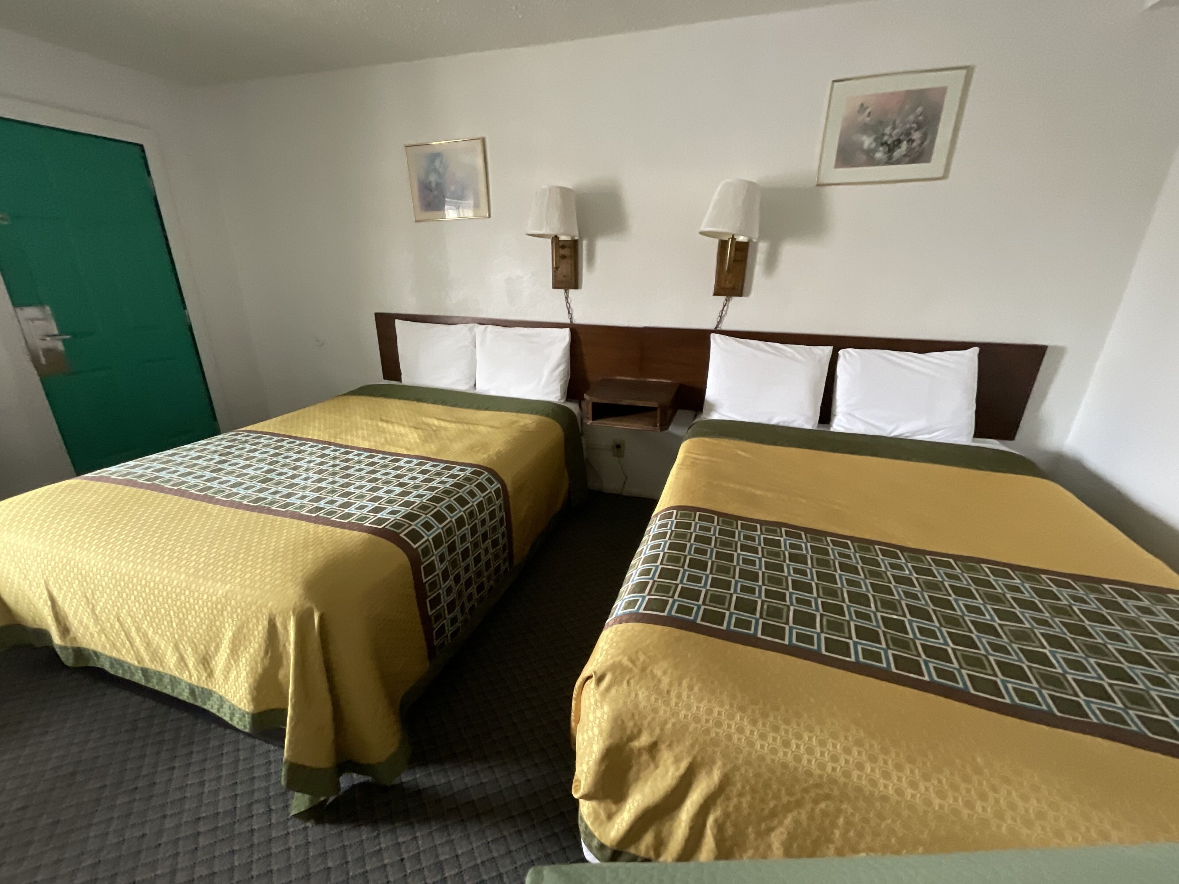 Habitación de hotel con dos camas, cada una con colcha estampada, cabecero de madera y dos lámparas de pared.
