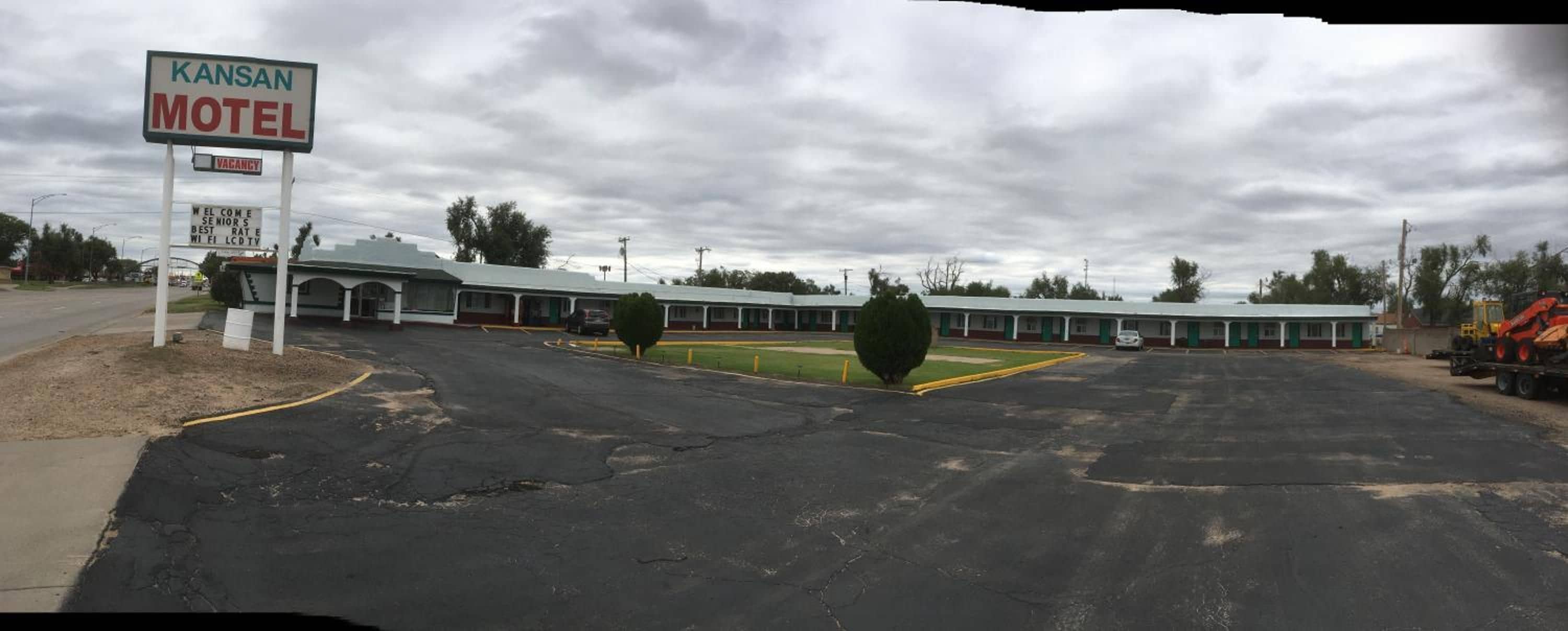 Un motel con un letrero que indica habitaciones disponibles, un estacionamiento y un edificio con techo plano.