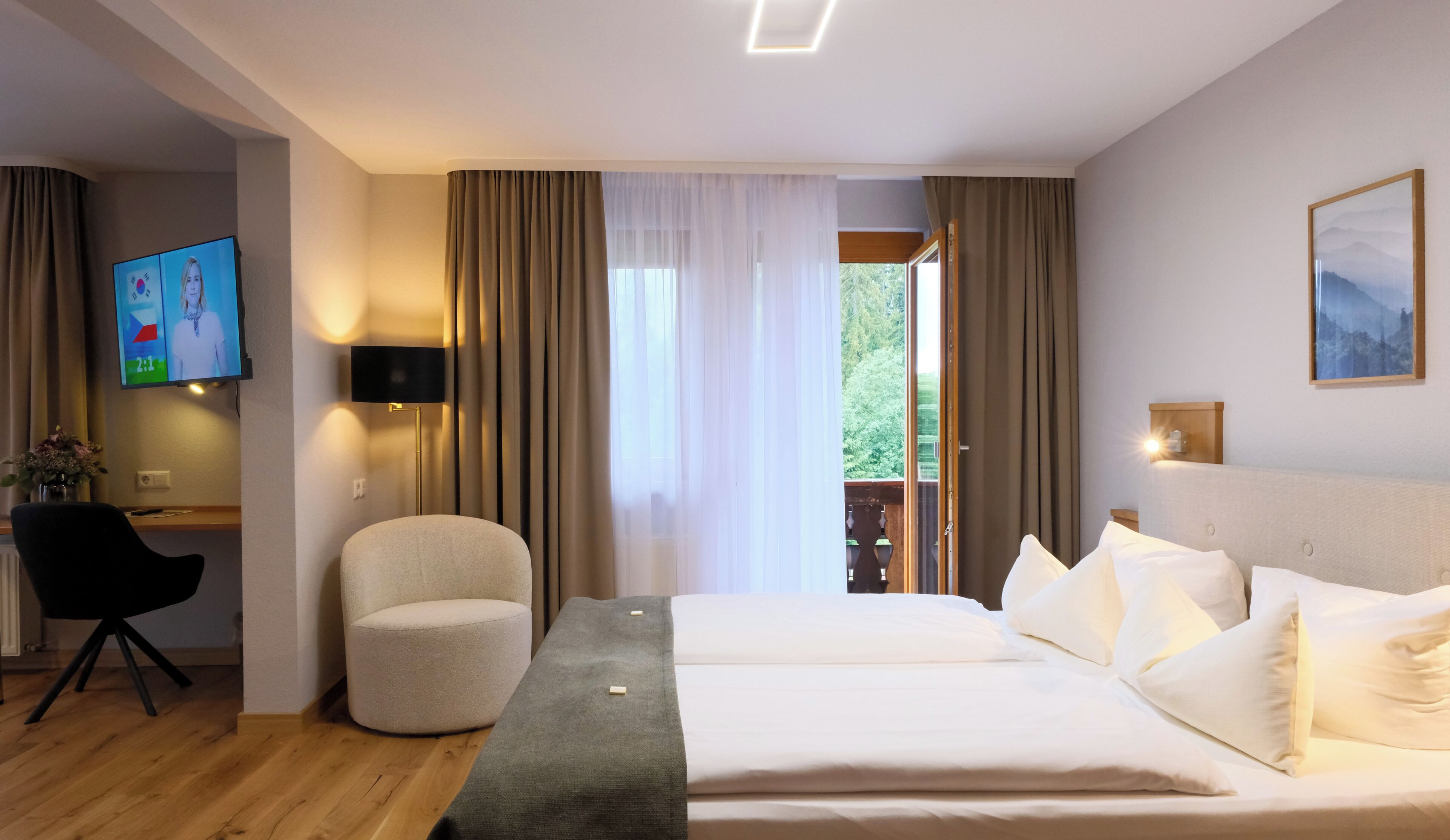 Een hotelkamer met een bed, een bureau met stoel, een televisie en een raam met gordijnen.