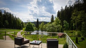 Un balcón con mobiliario exterior, vista a un lago y un paisaje boscoso.