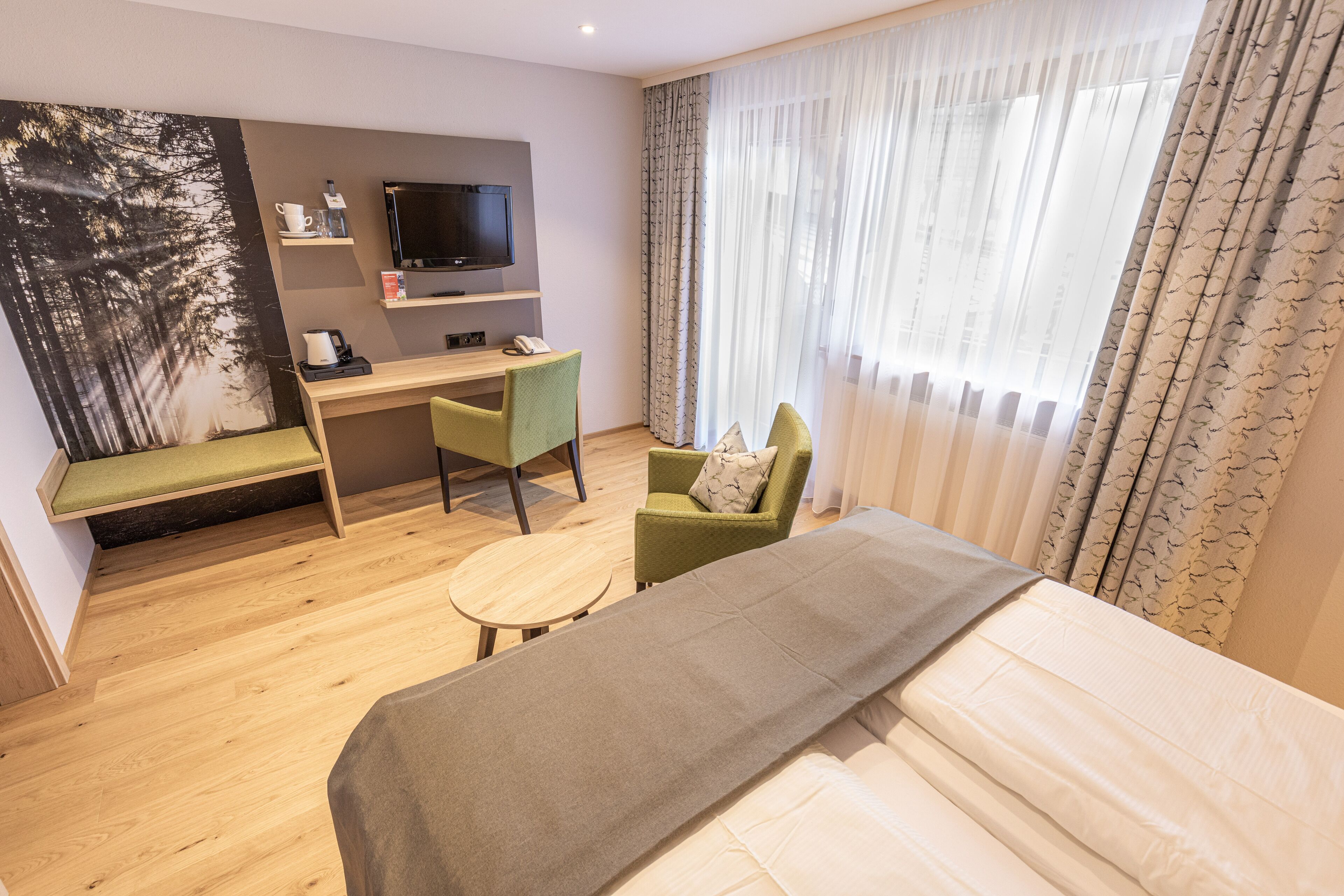 Habitación de hotel con cama, escritorio con silla, televisor y ventana con cortinas.