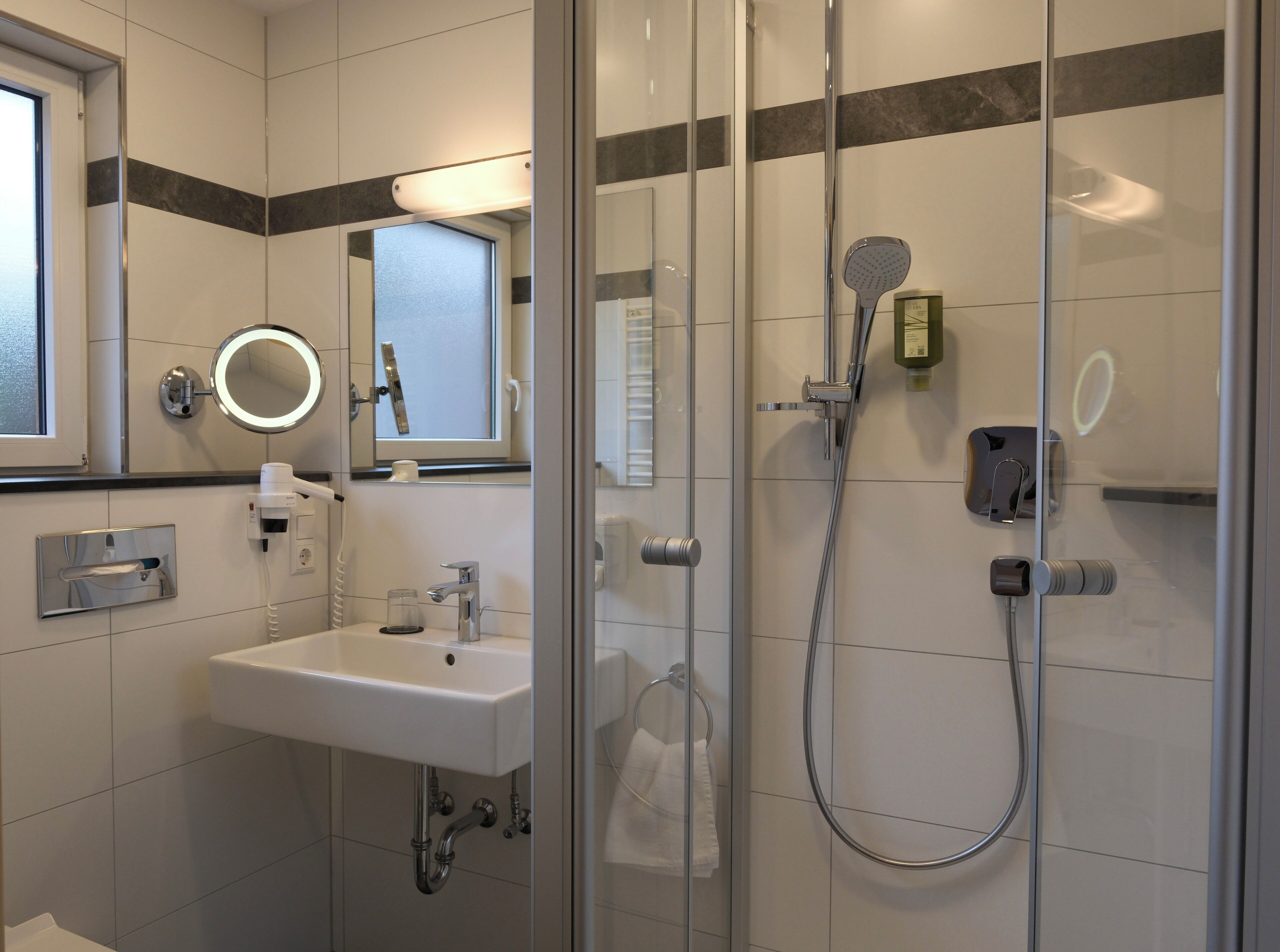 Une salle de bain moderne avec une douche à parois de verre, un lavabo blanc, un miroir et un porte-serviettes.