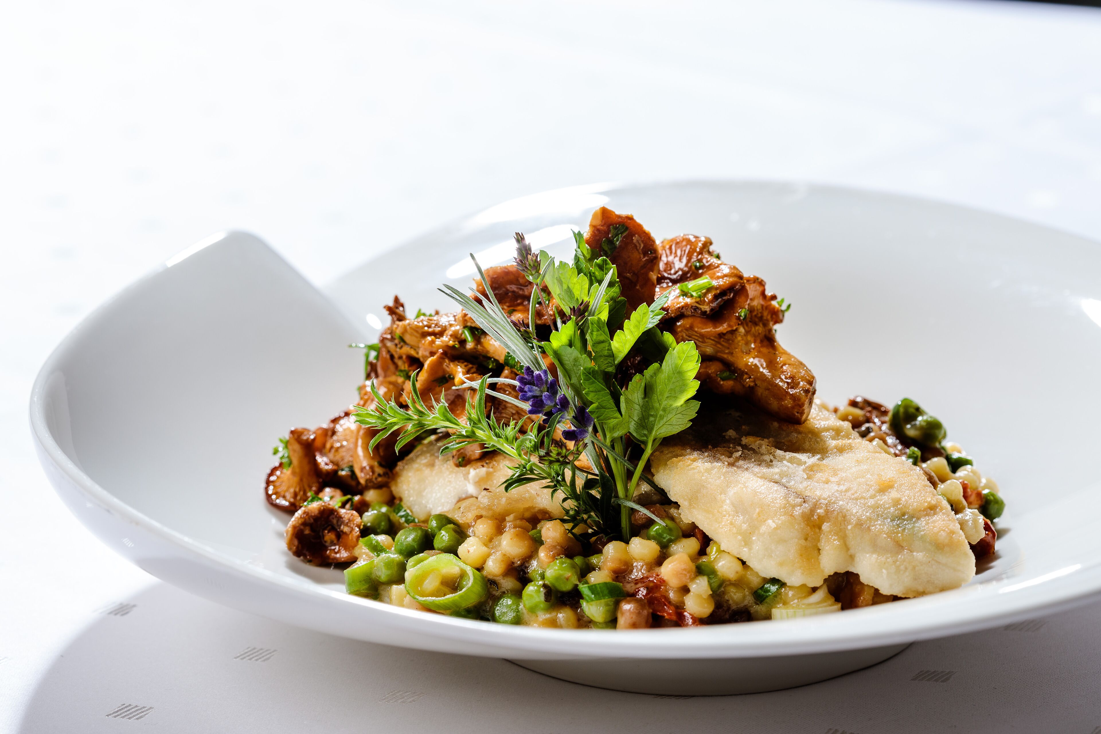 A white plate with a fish fillet, peas, and mushrooms, garnished with herbs.