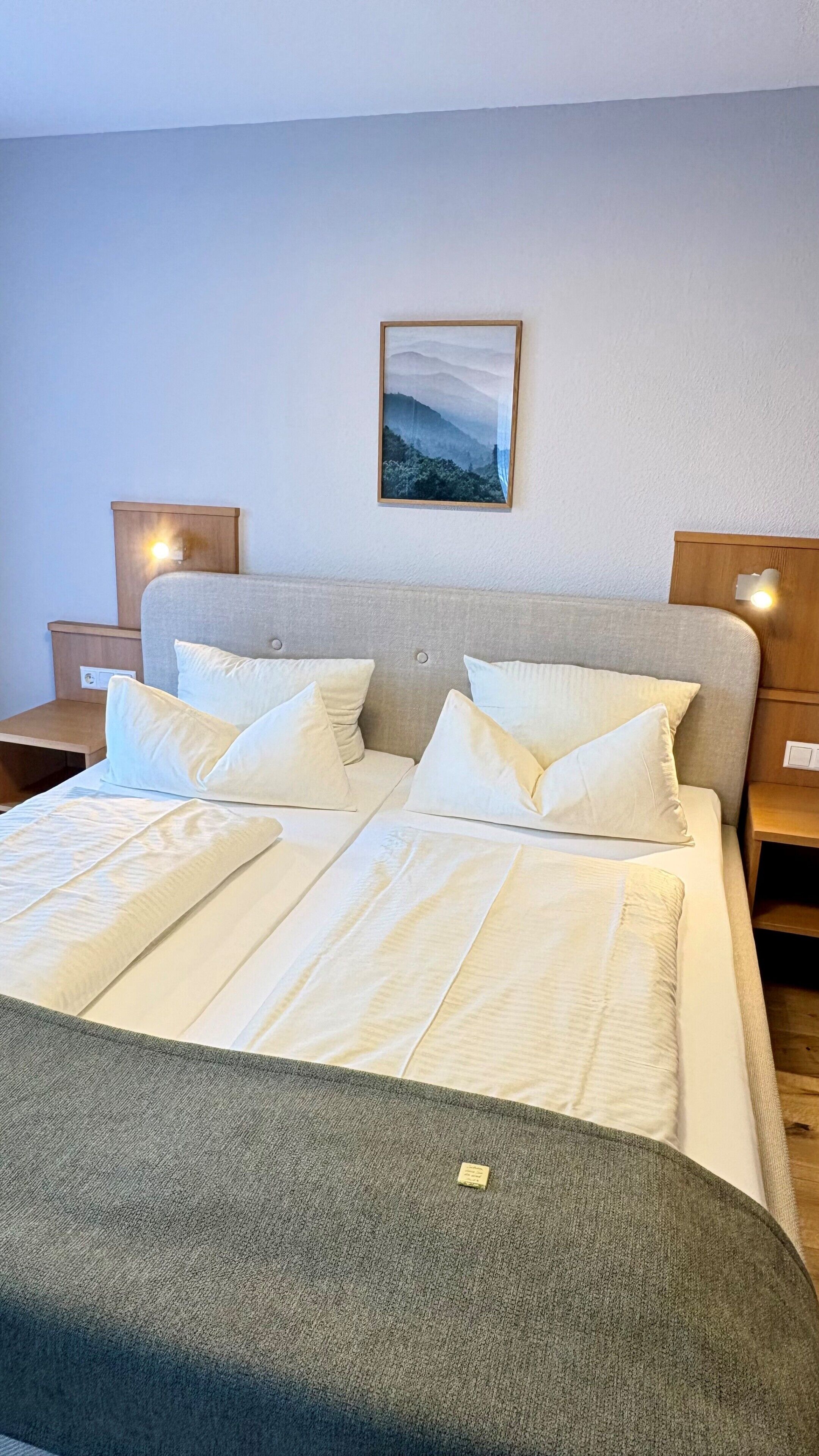 A neatly made bed with a grey blanket, a headboard, and a framed picture on the wall.