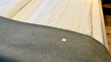 Una cama bien hecha con una manta gris, un cabecero y un cuadro en la pared.