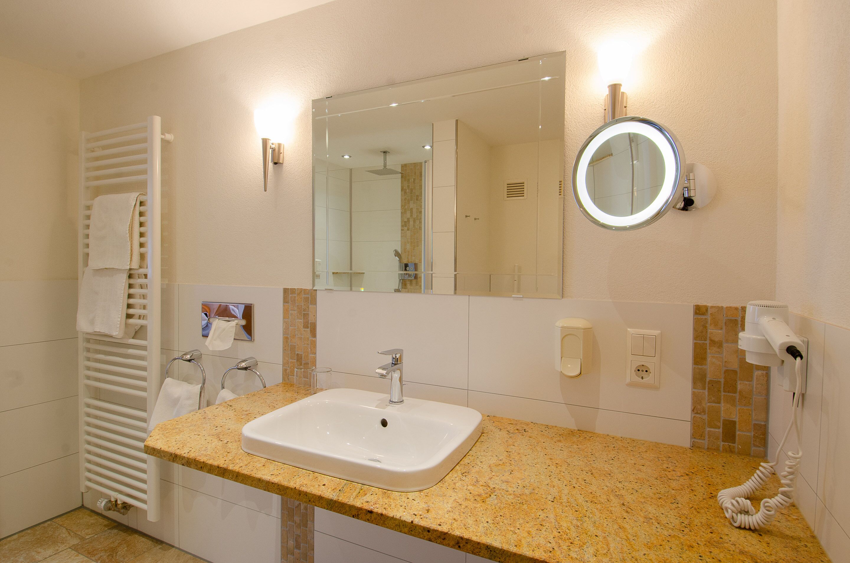 Un bagno con lavandino, specchio, portasciugamani e phon a parete.
