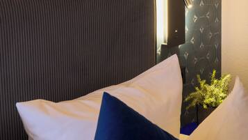 Una cama con almohadas blancas y azul oscuro, un cabecero oscuro y una pared con papel tapiz estampado.