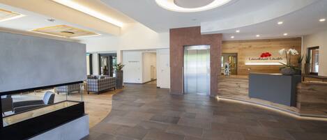 A spacious lobby with a reception desk, a wooden reception area, and a modern elevator.