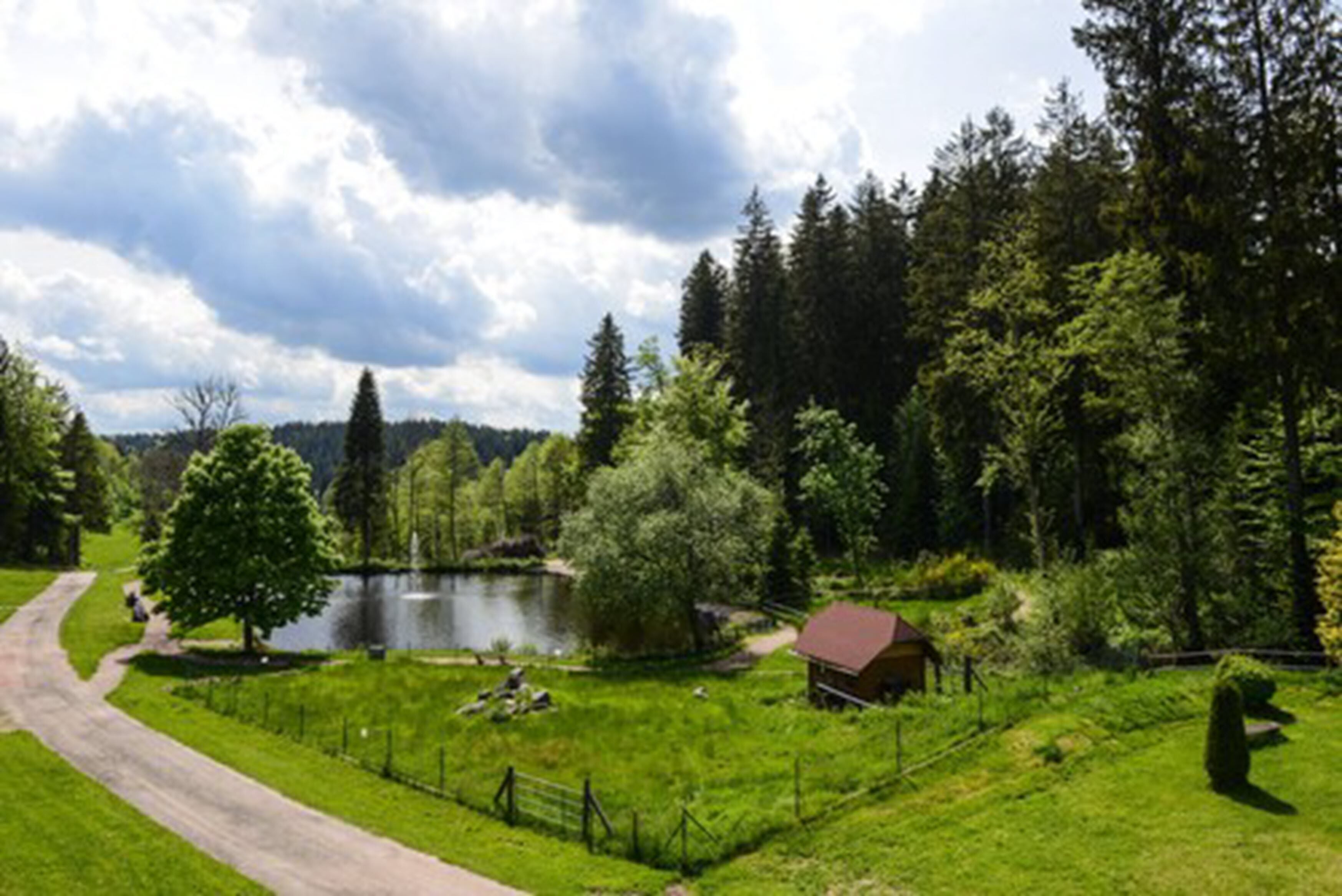 Un paisaje rural con un lago, una cabaña de madera y una zona cercada.