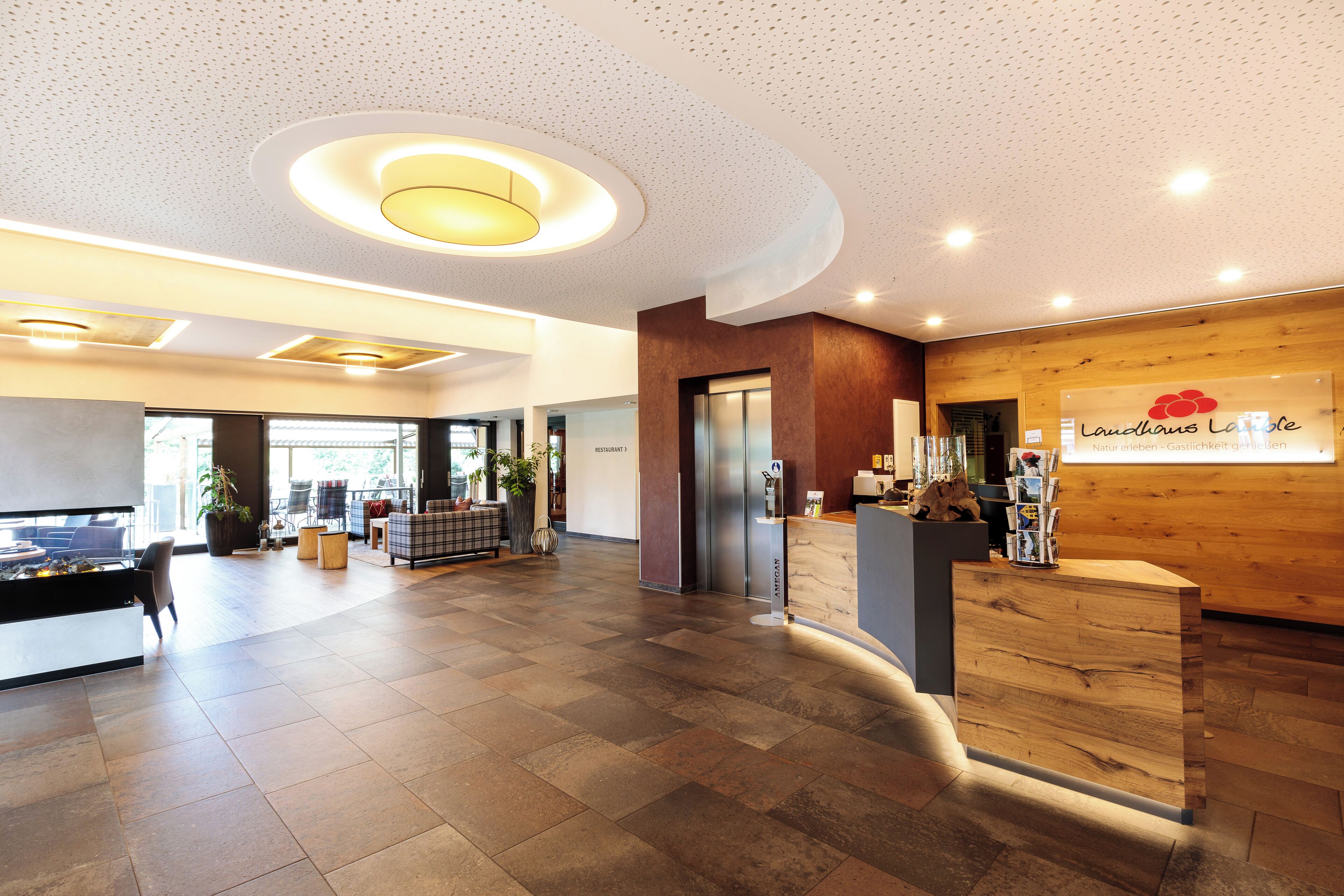 A spacious lobby with a wooden reception desk, a large plant, and a seating area with a fireplace.