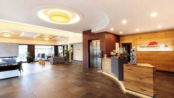 A spacious lobby with a wooden reception desk, a large plant, and a seating area with a fireplace.