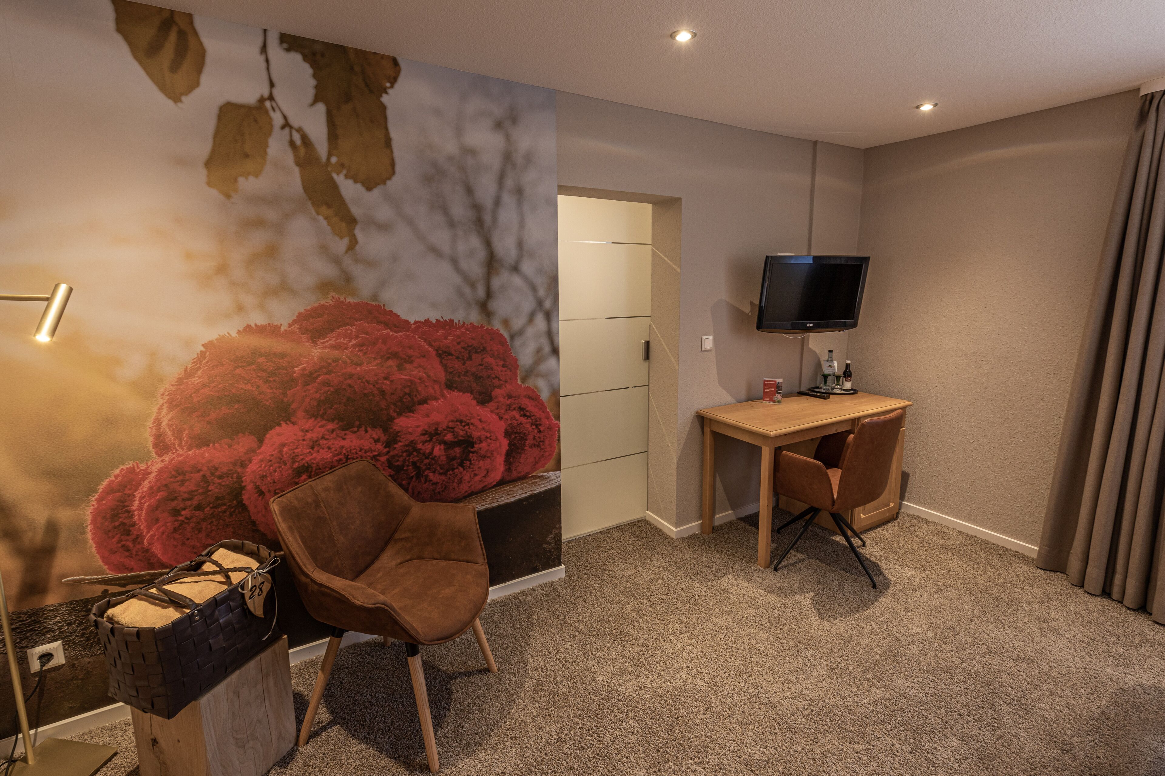A hotel room with a desk, chair, television, and a large wall mural.