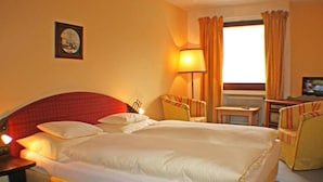 Quarto de hotel com uma cama grande, uma escrivaninha, uma cadeira e um abajur.