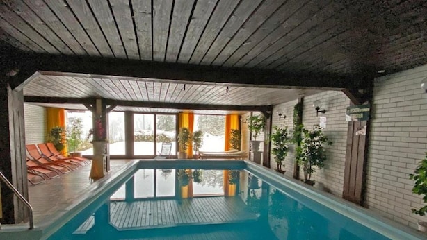 Piscina interior com vigas de madeira, chão revestido e vista para o exterior.