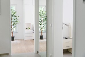 Een lichte, moderne kamer met een houten vloer, een witte dressoir, een bureau met lamp en twee potplanten.