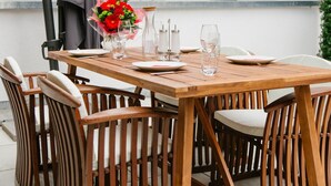 A wooden table set for four with white chairs, a bouquet of red flowers, and clear glassware. - Stadthaus Regensburg (Regensburg)
