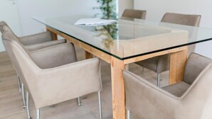 A modern dining table with a glass top and wooden base, surrounded by four beige upholstered chairs. - Stadthaus Regensburg (Regensburg)