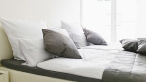 A bed with white and gray bedding, a window with blinds, and a white wall. - Stadthaus Regensburg (Regensburg)