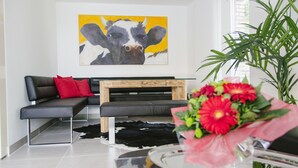 A modern living room with a black leather sofa, a wooden coffee table, and a cow painting on the wall. - Stadthaus Regensburg (Regensburg)