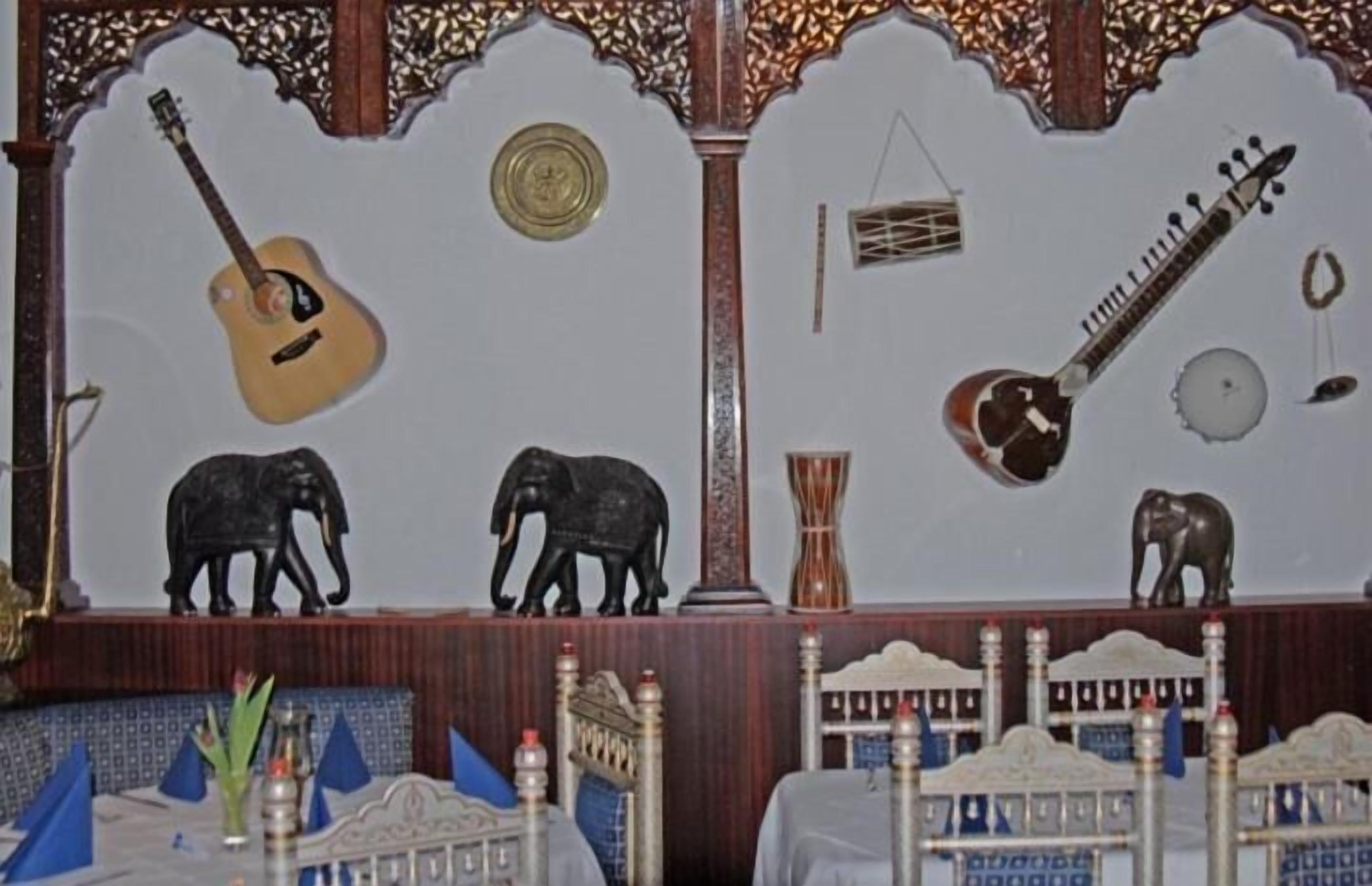 Una habitación de diseño tradicional, con una cama que tiene cabecera, una mesita con un florero y objetos decorativos como una guitarra y un sitar.